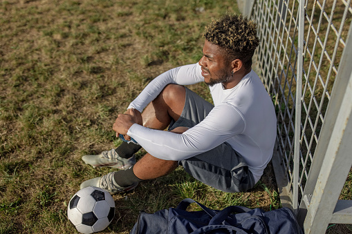A young African American man is sitting down and taking a rest from his soccer practise.