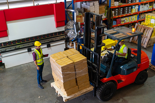 Caucasian foreman working together colleague in warehouse. Male worker driving forklift truck with pallet in factory construction site. Business industry engineering and manufacturing technology concept.