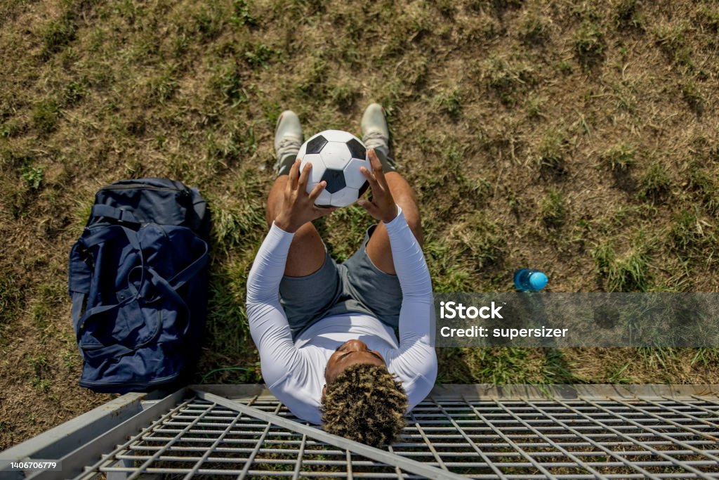 A quick break before I continue A young African American man is sitting down on the grass, while holding a soccer ball in his hands. 20-24 Years Stock Photo