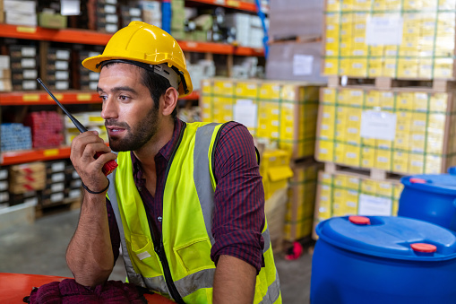 Stressed Caucasian man engineer talking on walkie talkie with colleagues in factory warehouse. Male worker working in construction site. Business industry and manufacturing technology concept.