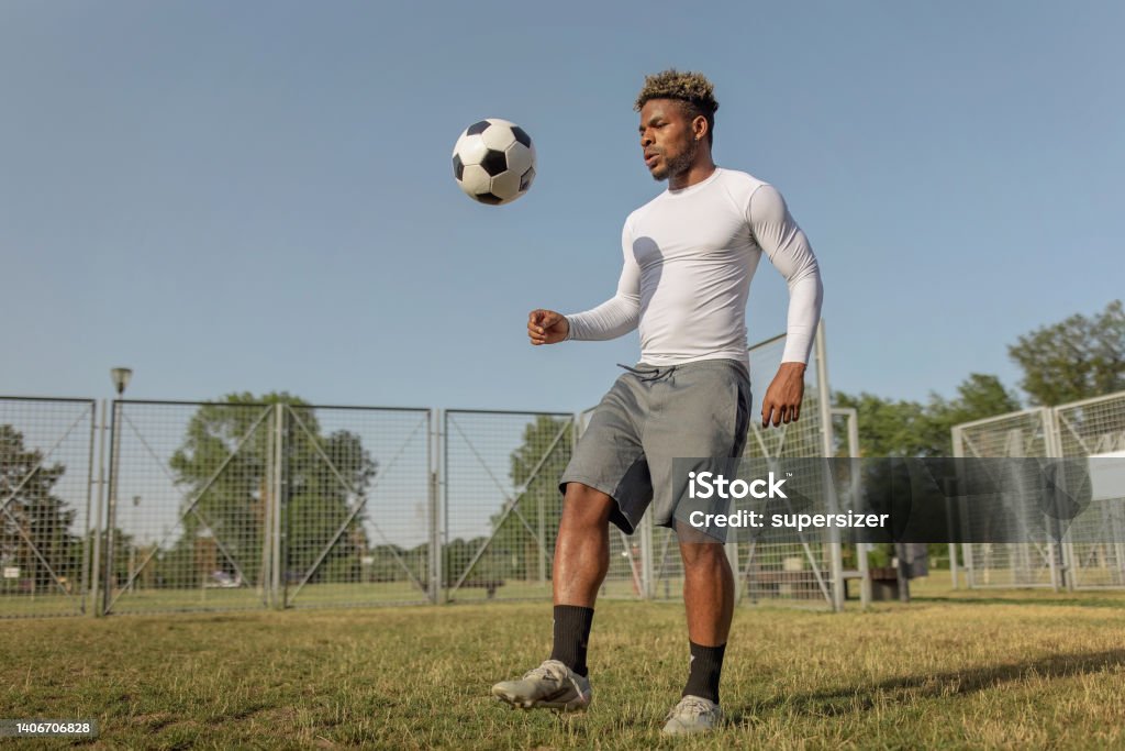 Practising every day is important A young African American man is wearing sports clothing while standing on a grass field and practising his kicks with a soccer ball. 20-24 Years Stock Photo