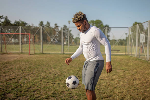 A young African American male wearing sports clothing is standing on a soccer field, practising his kicks.