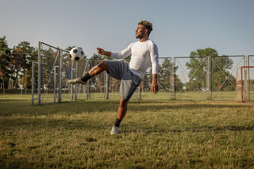 A young African American man is practising his kicks with a soccer ball, on a bright sunny day.