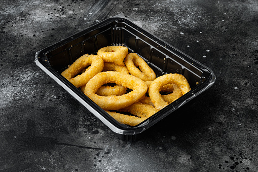 Frozen raw squid or onion rings breaded set, on black dark stone table background