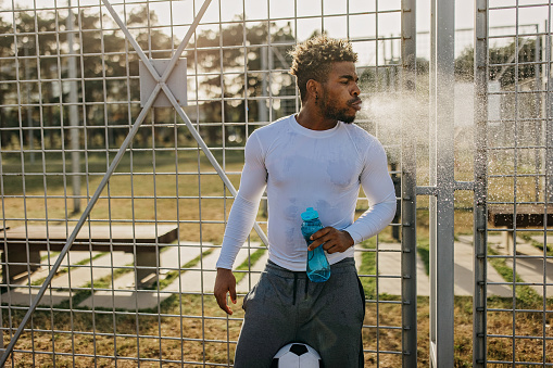 A young African American man is taking a water break and rinsing his mouth, spitting the water out.