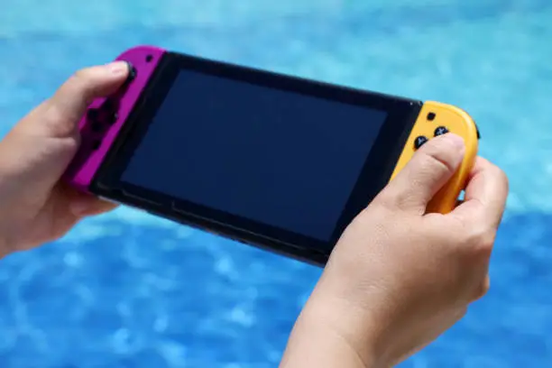 Photo of Woman playing game on handheld console near the  swimming pool, selective focus on hand
