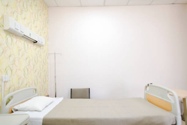 An empty bed prepared for the next patient, in a hospital room with accompanying equipment, next to the window.