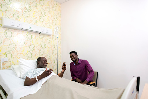 Young man using phone for medical insurance claim in hospital room with father