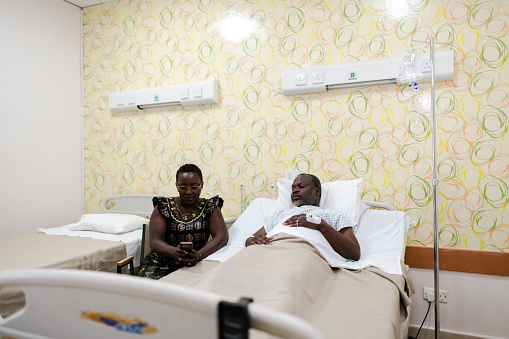 Woman using mobile phone in hospital ward with husband