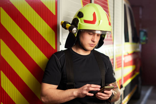 istock Portrait of a firefighter standing in front of a fire engine. Fireman using smart phone 1406712451