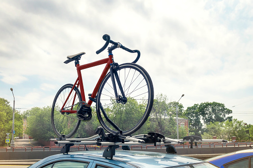 Red bicycle on blue car roof mounted with racks outdoors