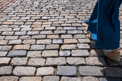 Cobblestone sidewalk. Woman's legs is walking forward on sunny day. Copy space for text.
