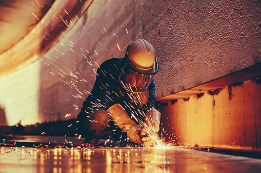 Trabajador masculino que corta la chispa de metal en la placa de acero del fondo del tanque con destello de luz de corte de cerca use guantes protectores y máscara photo