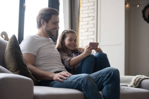 istock Young father and his daughter taking selfie while sitting on sofa at home 1406720034