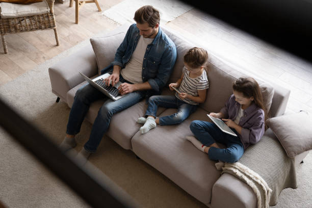 istock Young family of three holding and using different electronic devices while sitting on sofa in the living room 1406720051