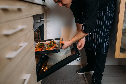 A happy professional cook preparing dinner, putting pork ribs into the oven.