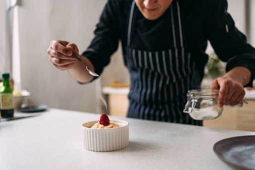 An anonymous professional cook preparing dessert, garnishing a raspberry crumble served in a white ramekin.