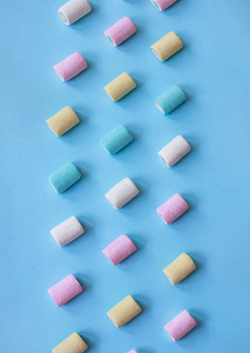 Colorful marshmallows arranged in a rows on blue background. Top view. Seamless pattern. Pastel colored.