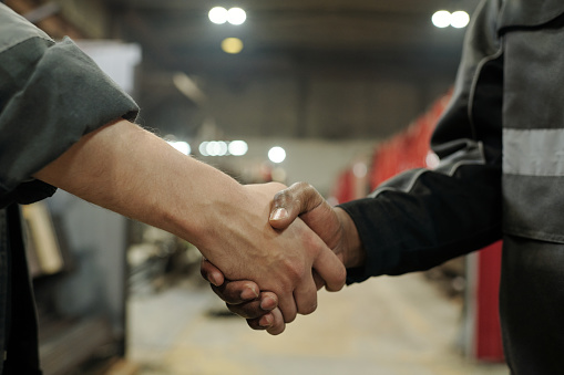 Handshake of two young intercultural workers of factory greeting each other after making deal or signing new contract of partnership
