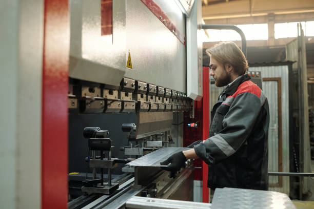 istock Side view of engineer in workwear putting metallic sheet on part of machine 1406725413