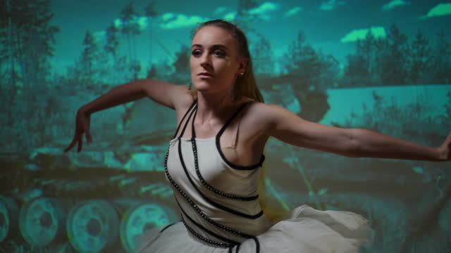 Portrait of confident young ballet dancer performing at background of destroyed tank picture. Concentrated serious Ukrainian performer dancing at demolished military vehicle photo. Art and victory.