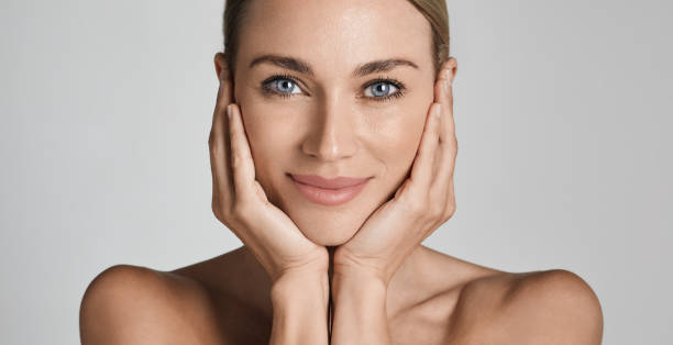 cuidado de la piel. hermosa mujer con piel facial sana tocando las manos hidratadas piel de la cara, sobre fondo gris claro. alta calidad - belleza natural fotografías e imágenes de stock