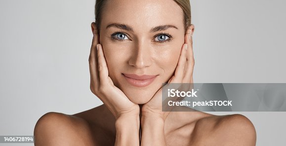 istock Skin care. Beautiful woman with healthy facial skin touching hands moisturized face skin, on light grey background. High quality 1406728194