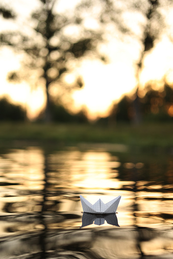 A paper boat is floating on the waves in the water at a beautiful sunset. Origami ship Sailing. The concept of a dream, future, childhood, freedom or hope