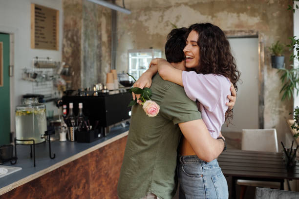 istock Young affectionate man embracing his cheerful girlfriend with pink rose 1406731432