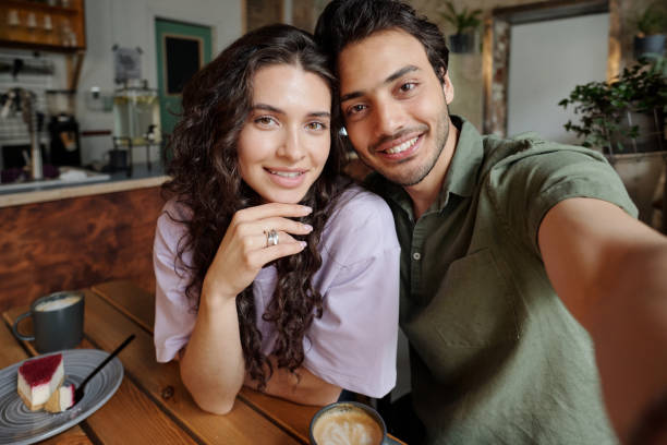 istock Young cheerful couple looking at smartphone camera held by smiling guy 1406731443