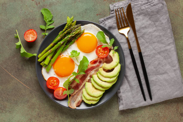 istock Tasty breakfast. Fried eggs with green asparagus, fried bacon on black plate on wooden table. Top view 1406735182