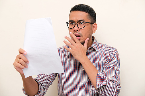 Adult Asian man showing shocked expression when read a letter