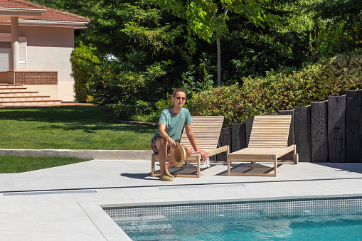 Young man sitting relaxed on a sun lounger in his garden pool on a hot summer day as leisure activity