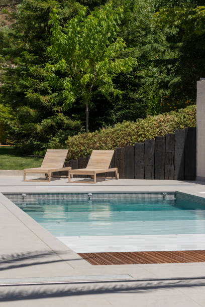 vertical view of swimming pool area in the garden of the house with wooden sun loungers and pool shutter - window sun sunlight vertical imagens e fotografias de stock