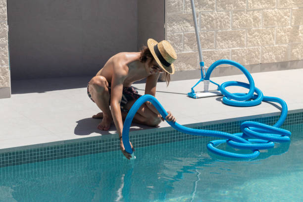 istock Young man wearing a hat crouched connecting the blue plastic pipe for the electric swimming pool cleaner 1406741349