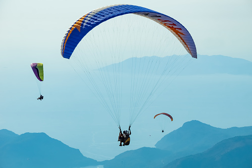 Paragliding in the sky. Paraglider tandem flying over the sea with mountains at sunset. Aerial view of paraglider and Blue Lagoon in Oludeniz, Mugla, Turkey.