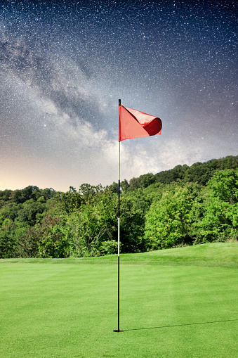 A golf flag in the hole on a putting green with a composite starry night sky.