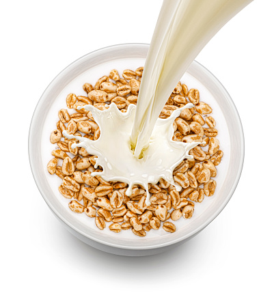 Puffed wheat cereal with pouring milk isolated on white background, top view