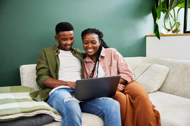 istock Smiling young couple using a laptop on their living room sofa 1406752821