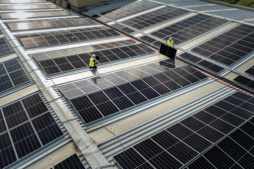 Team of engineers using technology while installing solar panels on a roof of warehouse.
