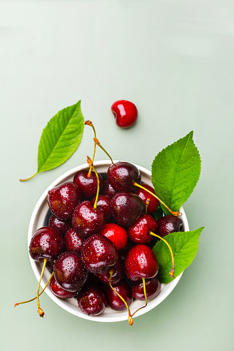 Juice and fresh cherry with leaf and water drops on green background. Sweet red berry cherries on bowl. Summer fruit Background