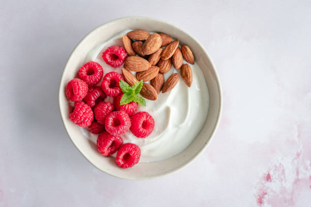 Bowl of yoghurt with raspberries and almonds on a light pinkish background Overhead view of a bowl of yoghurt with raspberries and almonds on a light pinkish background greek yogurt photos stock pictures, royalty-free photos & images