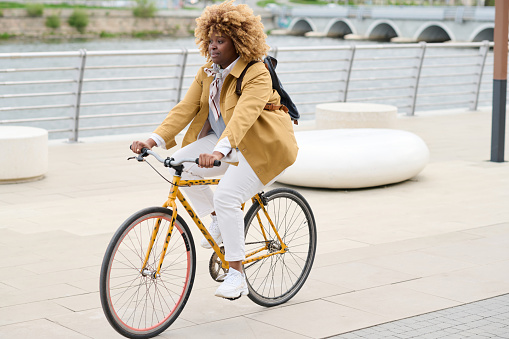 African young woman with curly hair riding on a bike along the street in the city
