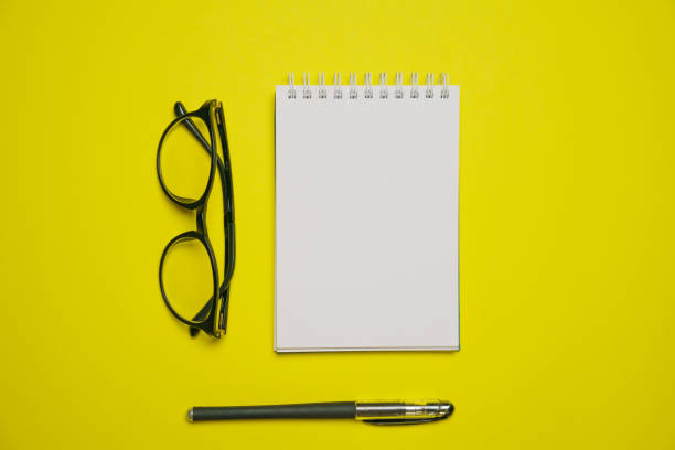 istock Minimal composition with blank blaktoth, glasses and pen on yellow table, flat 1406763520