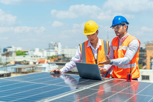 Engineers discussing project of solar power station. Solar panel technician on roof. Engineer and Young technician installing solar panels on factory roof. stock photo