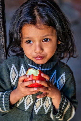 Happy little Nepali girl eating an apple, she lives in Bhaktapur.