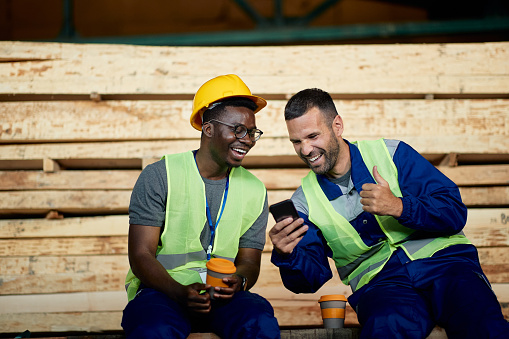 African American worker and his colleague laughing and having fun while using smart phone during their coffee break.