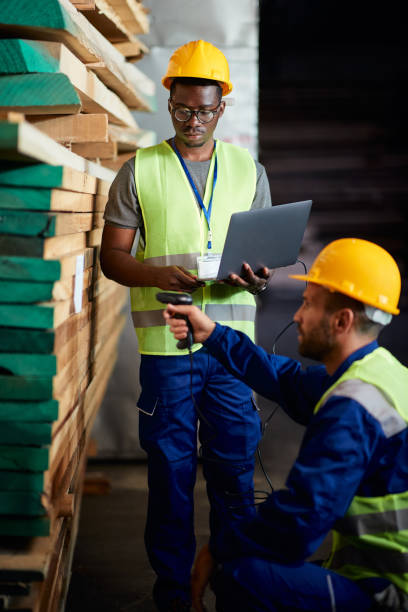 istock Black worker and his colleague scanning labels on timber planks while working in a warehouse. 1406766305