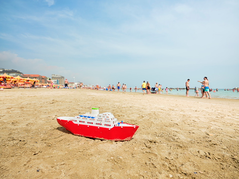 Toy cruise ship on an Italian beach on a sunny summer morning with people in the back as they cool off by the sea. Children's toy on the Adriatic sea, Italy.