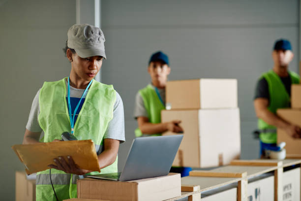 istock Black female worker scanning packages and using laptop while working at distribution warehouse. 1406767398